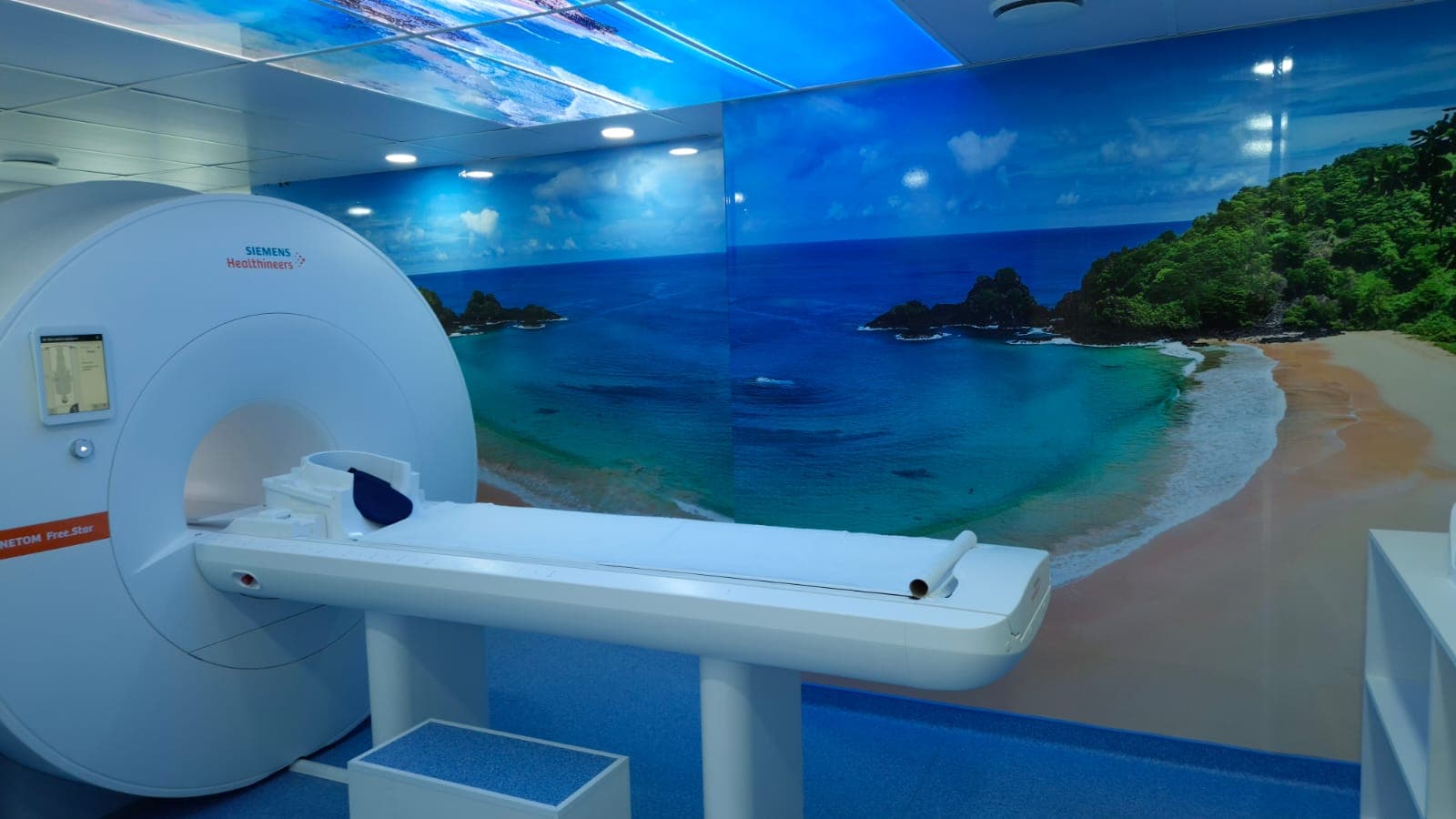 Sala de ressonância magnética do Instituto Wilson Rosado com a mesa de exame e o mural da praia