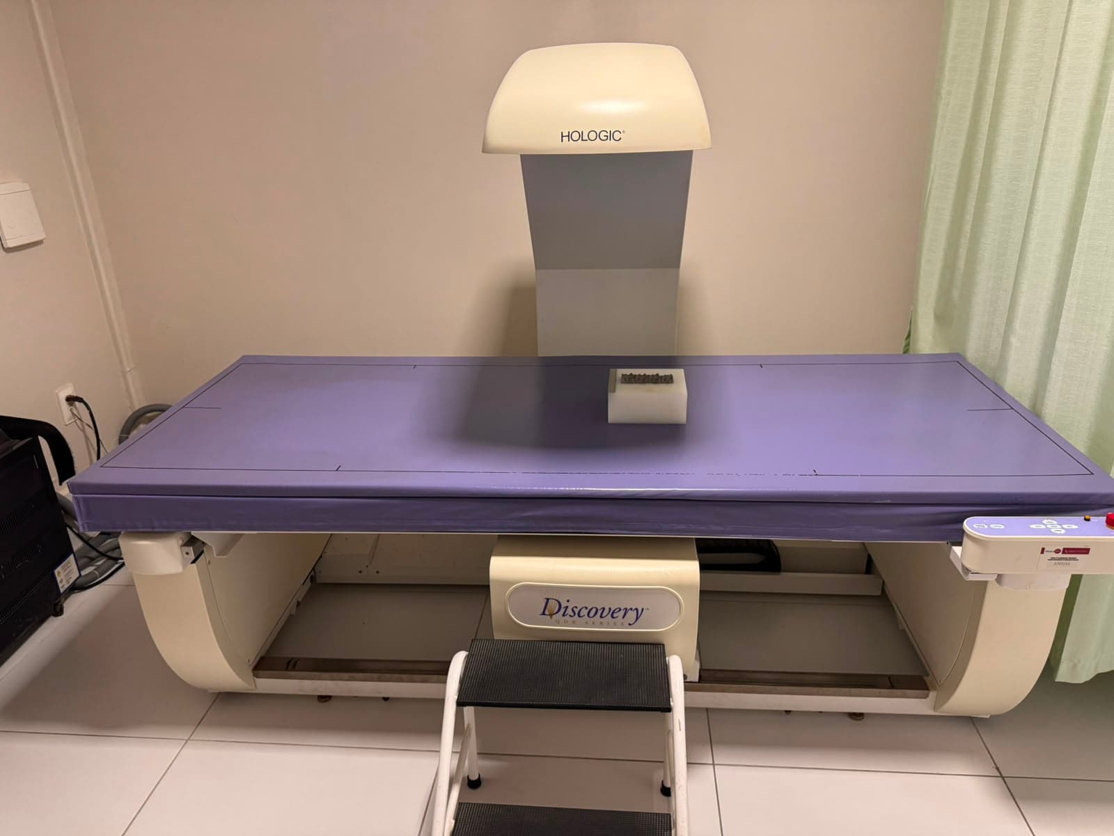 Densitômetro Hologic Discovery visto de frente, com a mesa de exame e o degrau de acesso